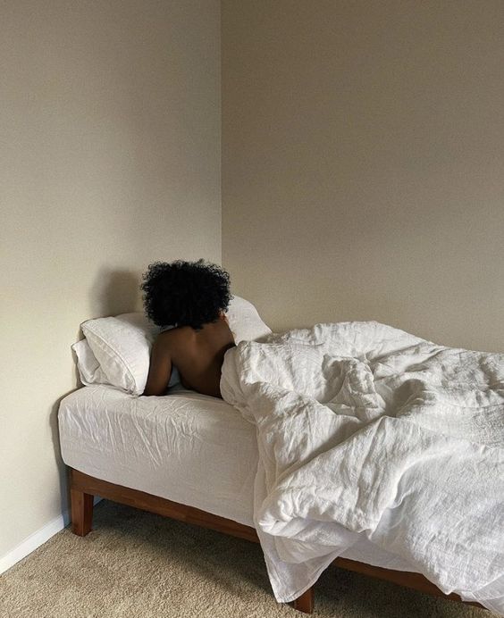 Black woman laying in an all white bed